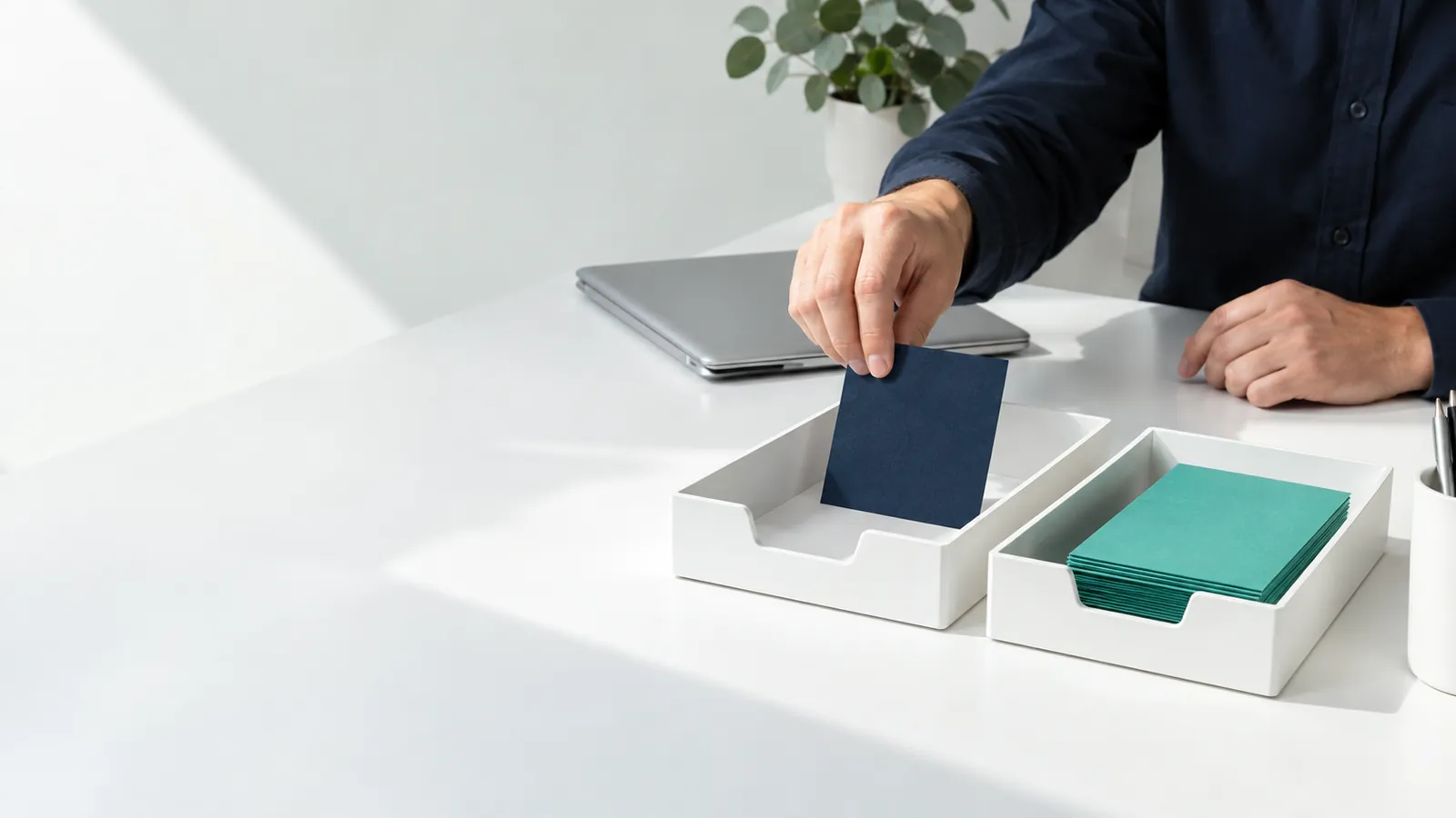 Les mains d'un employé déposent une carte bleu nuit dans une corbeille blanche, à côté d'une pile de cartes vertes déjà traitées
